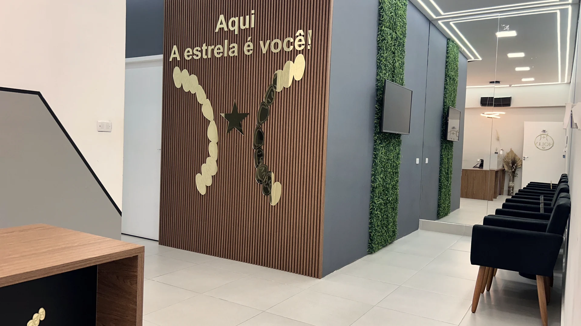 Corredor da Clínica Holly com painel ripado e a frase Aqui a estrela é você, jardim vertical e poltronas de espera