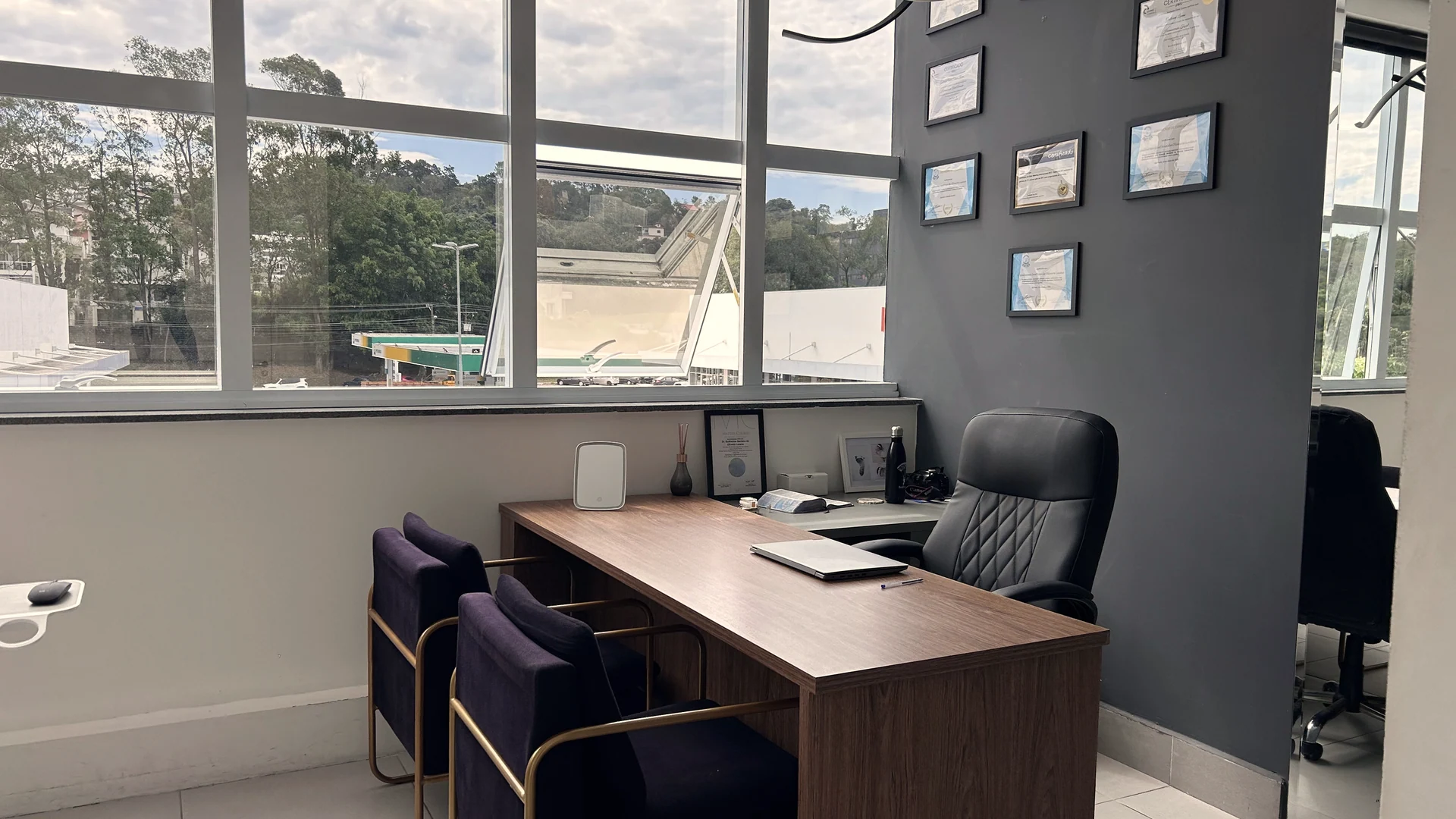 Sala de planejamento da Clínica Holly, com mesa de madeira, poltronas e certificados na parede, diante de janelas amplas