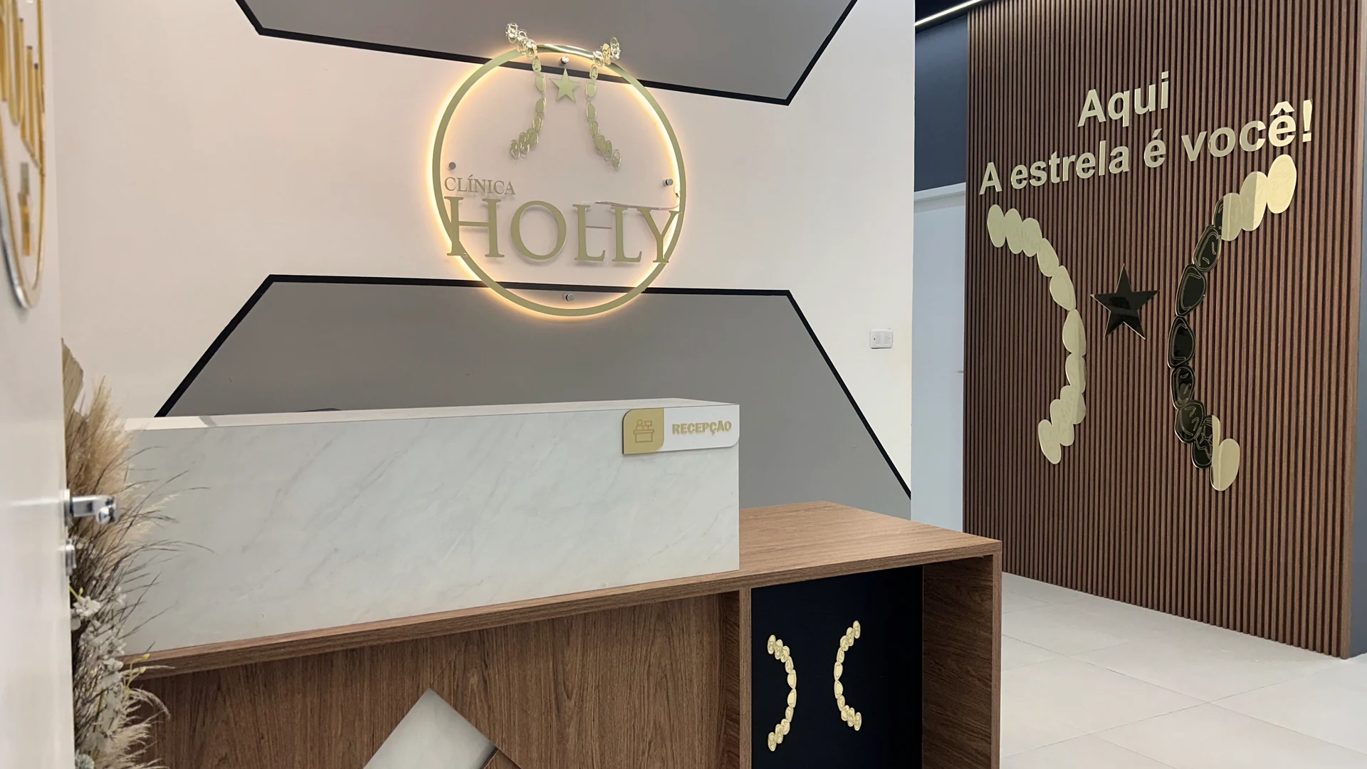 Recepção da Clínica Holly, com balcão em mármore e madeira e o logotipo iluminado na parede